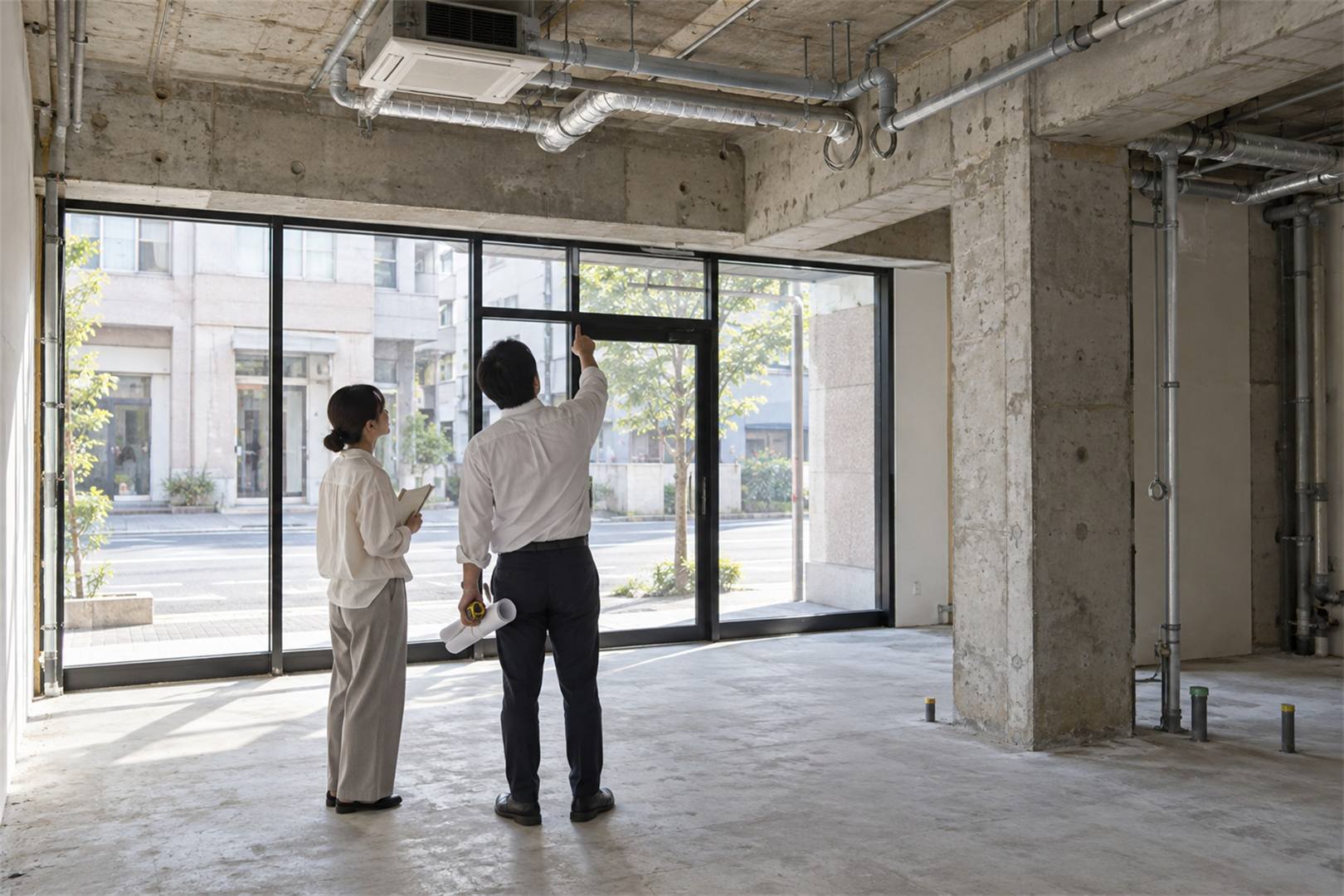 契約前の空きテナントで、梁と柱を見上げて確かめる建築士とお客さま